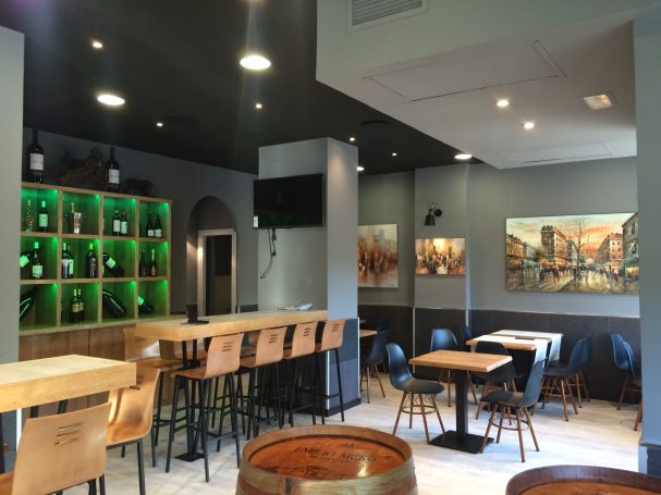 Interior de un bar moderno con una barra de madera, mesas y una decoración en tonos oscuros.