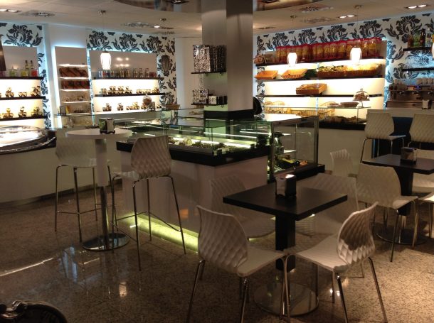 Interior de una cafetería moderna con mesas, sillas y vitrinas de postres.