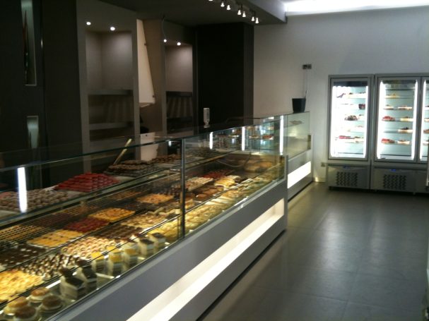 Interior de una heladería con vitrinas llenas de helados y un congelador al fondo.