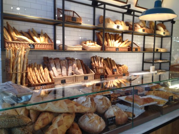 Panadería con estantes llenos de diferentes tipos de pan y productos de pastelería.