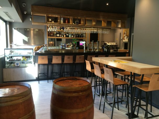 Bar decorado con barriles de madera, mesas y sillas modernas. Ambiente acogedor y luminoso.