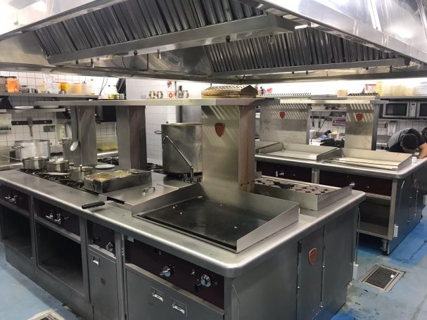 Cocina industrial equipada con varias estufas, freidoras y una campana extractora.