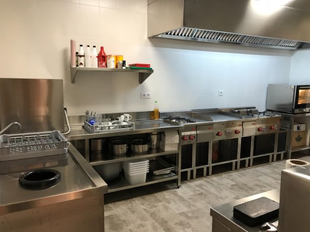 Cocina moderna con estantes, fogones y electrodomésticos de acero inoxidable.