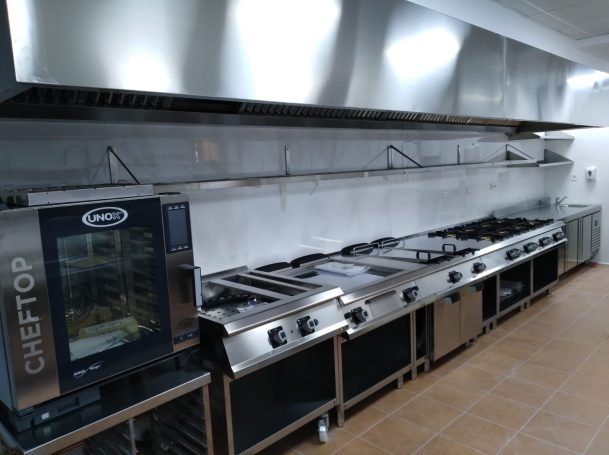 Cocina industrial equipada con fogones, campana y horno.