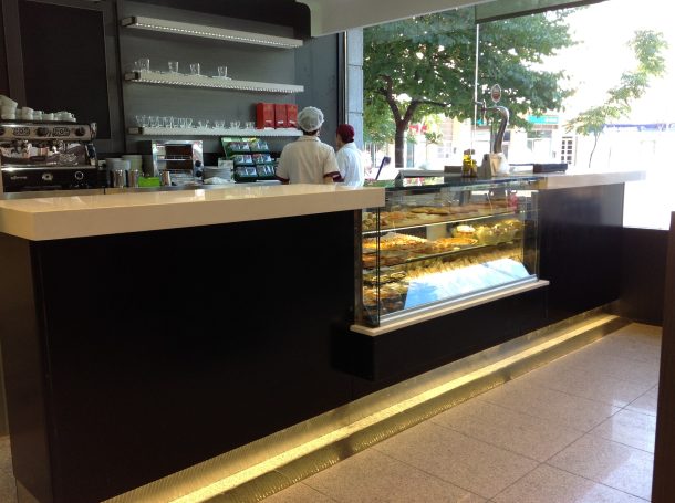 Barra de café con repostería expuesta y personal trabajando en un entorno luminoso.