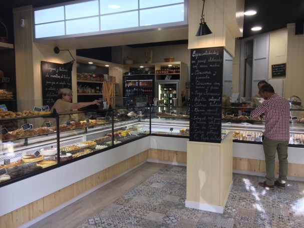 Panadería con estantes llenos de productos y clientes eligiendo postres y panes.