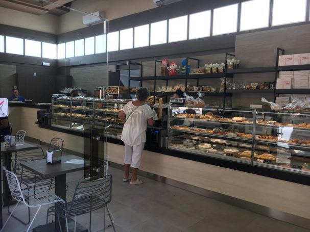 Una persona elige pasteles en una panadería moderna con vitrinas de exhibición.