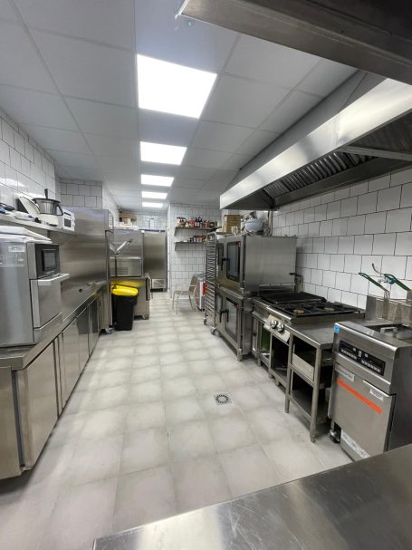 Cocina industrial equipada, con mesas de acero y electrodomésticos en un ambiente ordenado.