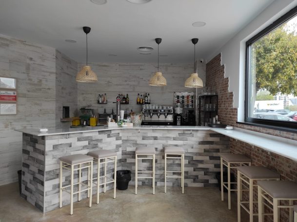 Bar moderno con asientos altos, decoración de piedra clara y ventanales grandes.